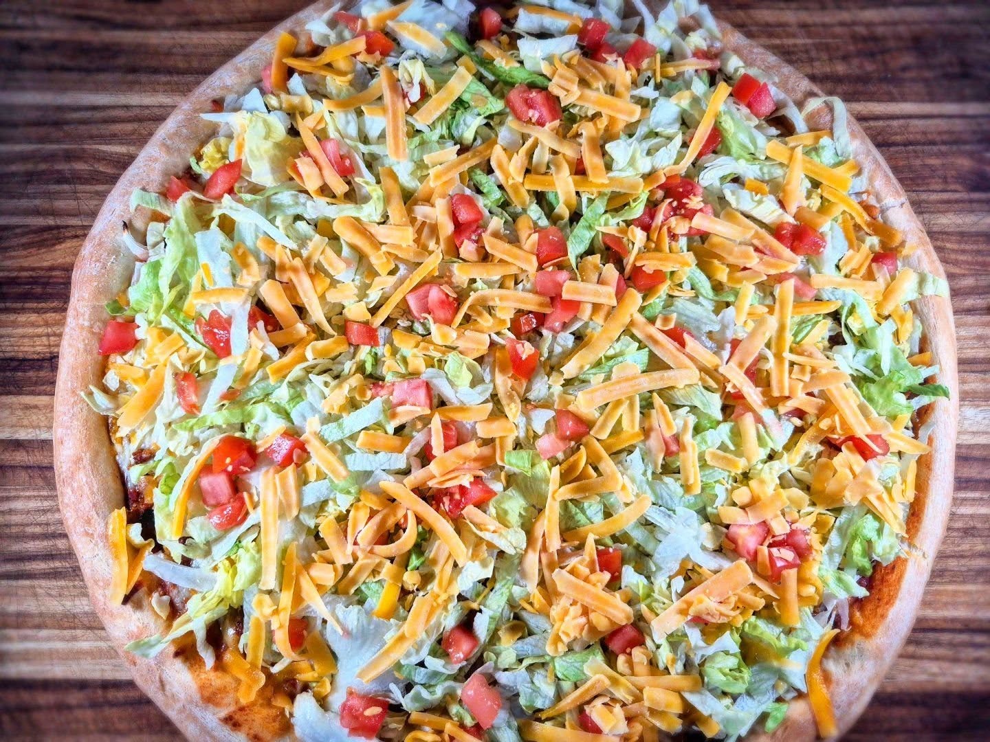 Taco pizza topped with lettuce, tomatoes, and shredded cheddar